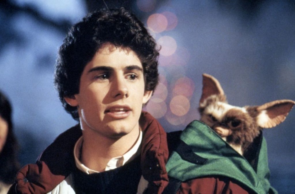 Zach Galligan as Billy Peltzer standing with Gizmo the Mogwai peeking out of his rucksack in the 1984 Christmas horror classic Gremlins.