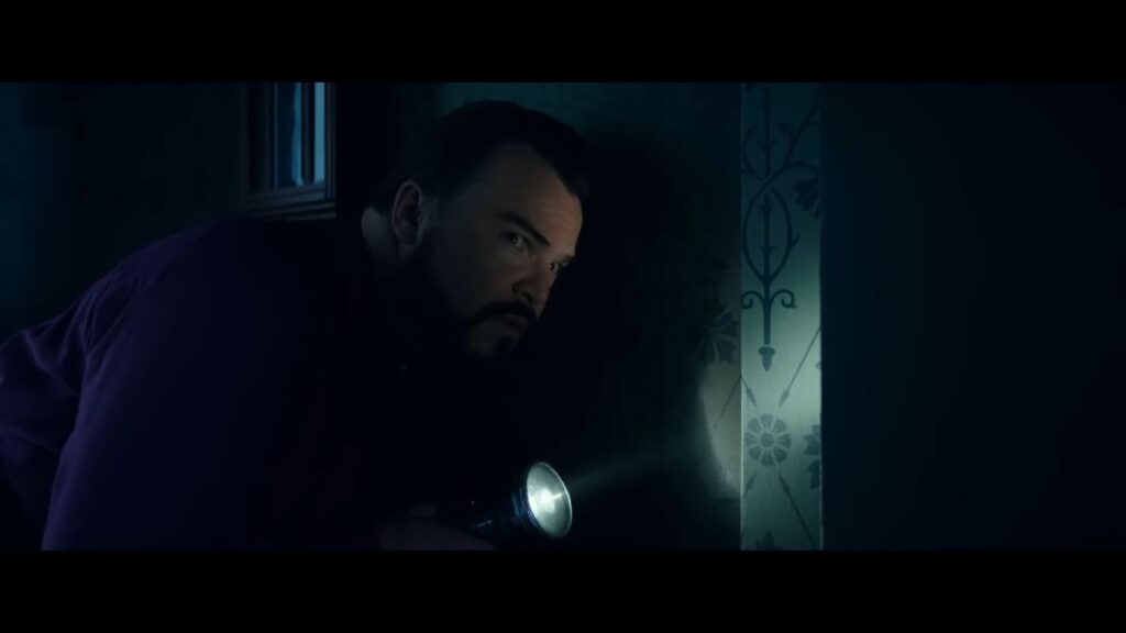 Jack Black uses a torch to investigate a dark, patterned wall in the children's horror movie The House with a Clock in Its Walls (2018).