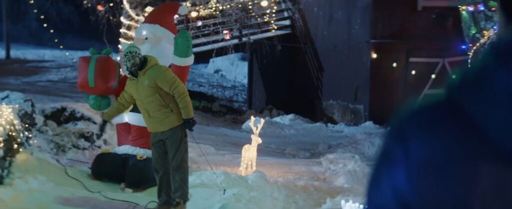 A terrified man standing next to a large inflatable Santa decoration in the snow in the Norwegian horror-comedy There's Something in the Barn.
