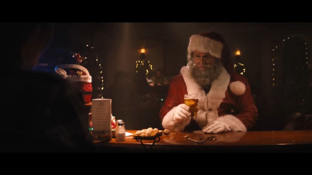 David Harbour as a gritty, exhausted Santa Claus drinking a beer at a bar in the action-horror movie Violent Night.