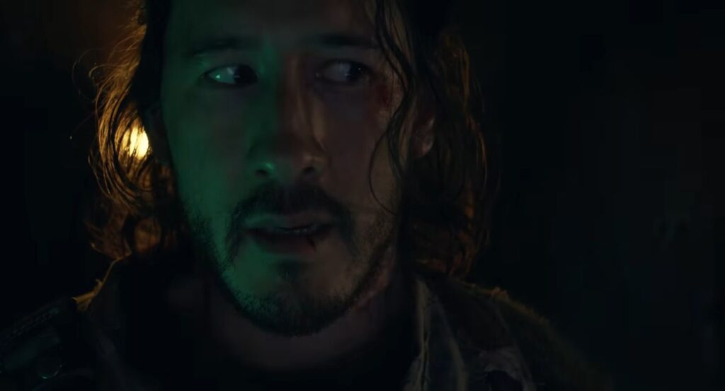 Writer and director Mark Fischbach (Markiplier) looks on with a bloodied face and a concerned expression in a dark, atmospheric still from the movie Iron Lung.