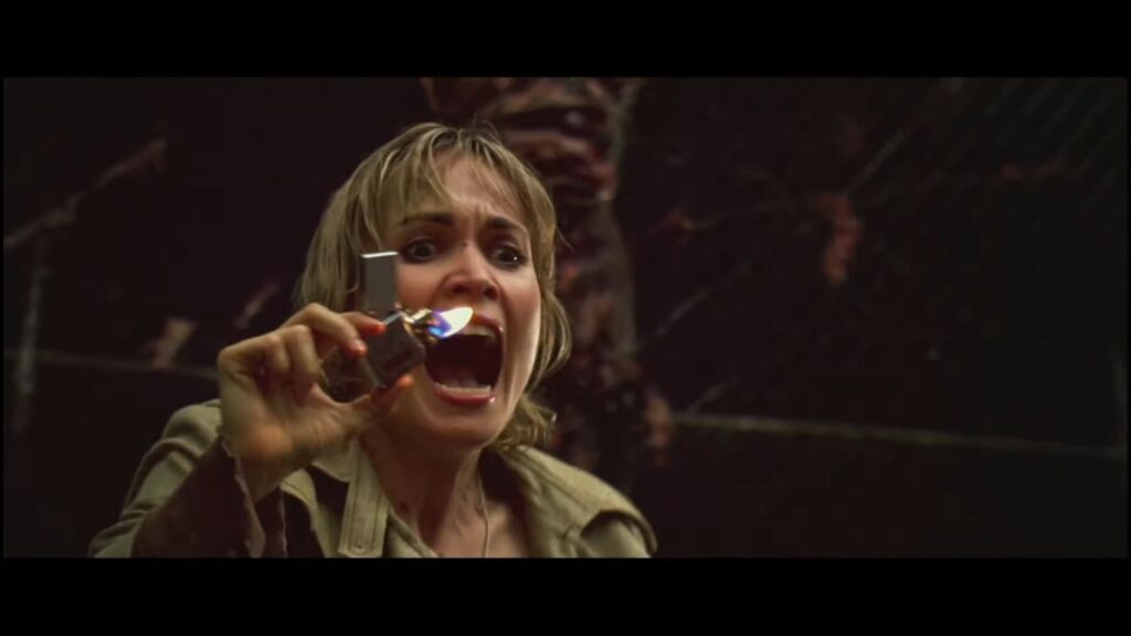 Radha Mitchell as Rose Da Silva screams while holding up a lit lighter in the foggy, dark underworld of the Silent Hill (2006) film.