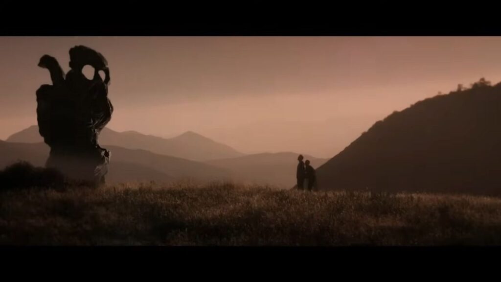 The Endless (2017): Two figures silhouetted against a vast, eerie mountain landscape featuring a strange, impossible monolith under a hazy sky.