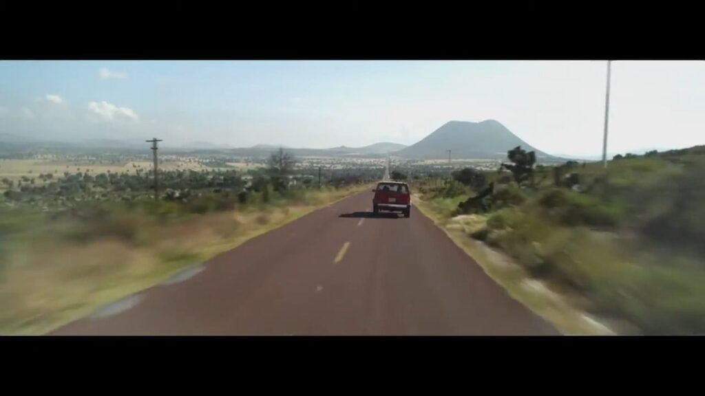The Incident (2014): A lone red car driving down a never-ending, empty desert highway toward a distant mountain, representing an infinite road loop.