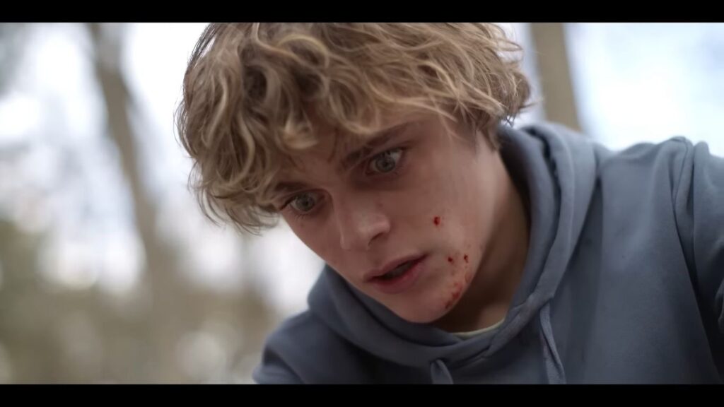 A blonde teenage boy with blood on his cheek and a panicked, distressed expression in Bring Her Back.