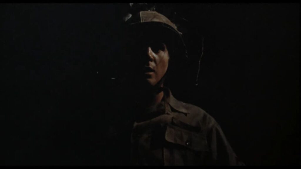 A soldier wearing a military helmet stands in near-total darkness, his face partially illuminated by a stark light source in the horror film Dead of Night (1974).