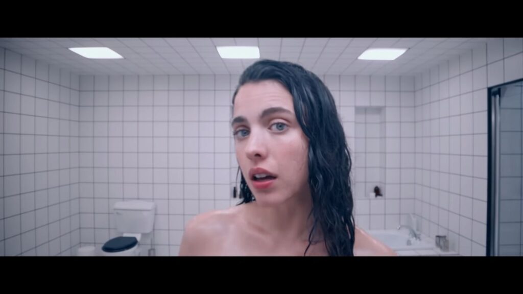 Margaret Qualley with dark, wet hair looking directly into the camera in a white tiled bathroom in The Substance.