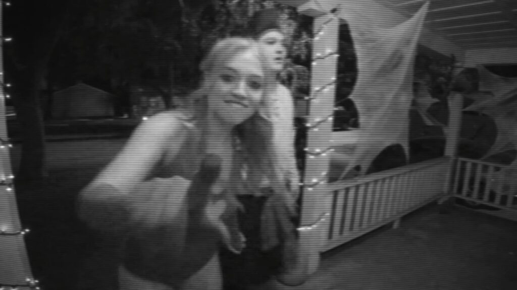A grainy, black-and-white VHS-style security camera shot of young people outside a decorated house in V/H/S/Halloween.