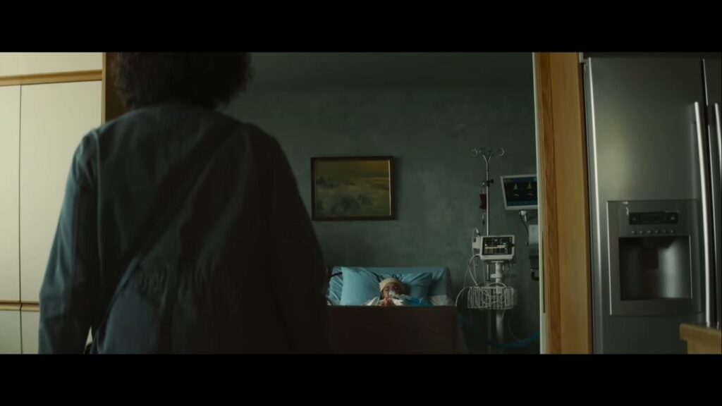 The silhouette of a woman walking into a clinical hospital room where a young patient is hooked up to medical machinery and an IV in the horror movie Birth/Rebirth.